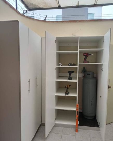 Un armario de almacenamiento abierto con estantes, herramientas eléctricas y una bombona de gas en un espacio similar a un garaje.