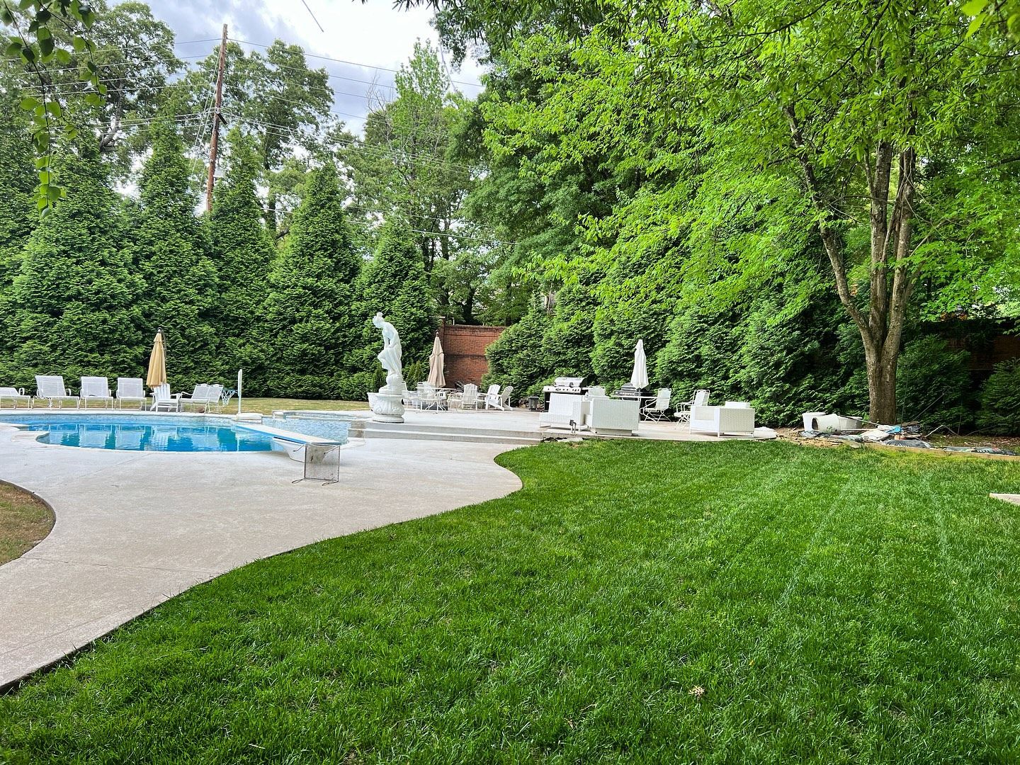 Backyard with pool, white furniture, statues, and green lawn. Trees in the background.