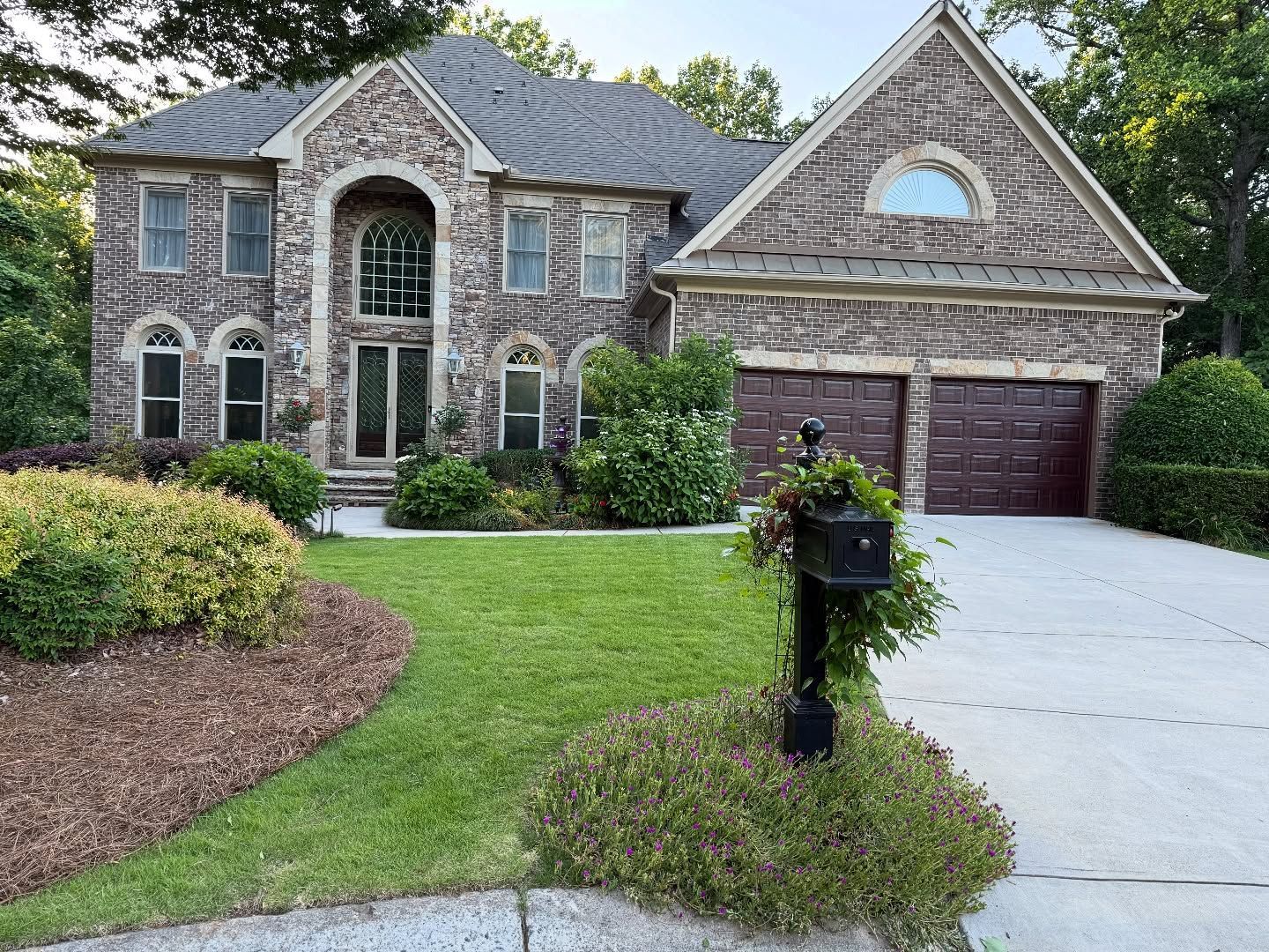 Two-story brick house with green lawn, landscaping, and a mailbox.