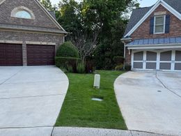 Two brick houses with driveways, separated by a green lawn and a small utility box.