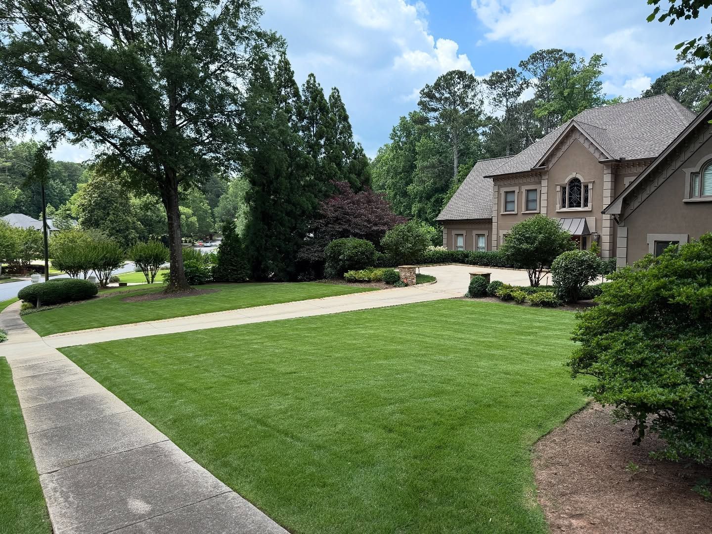 A well-manicured lawn and house with a long driveway on a sunny day.