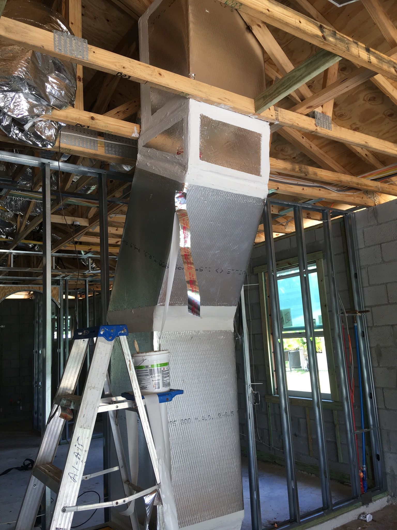 Metal HVAC ductwork being installed in a house under construction. A ladder is positioned below.