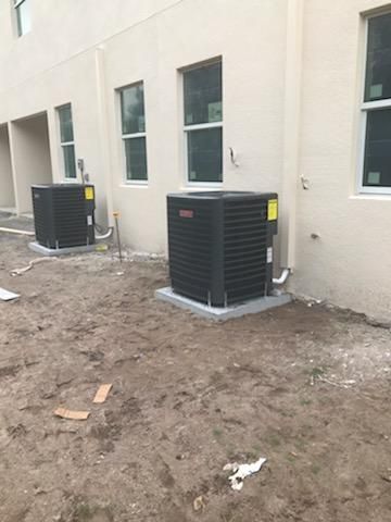 Two black AC units outside a light-colored building, set on concrete pads, dirt ground.