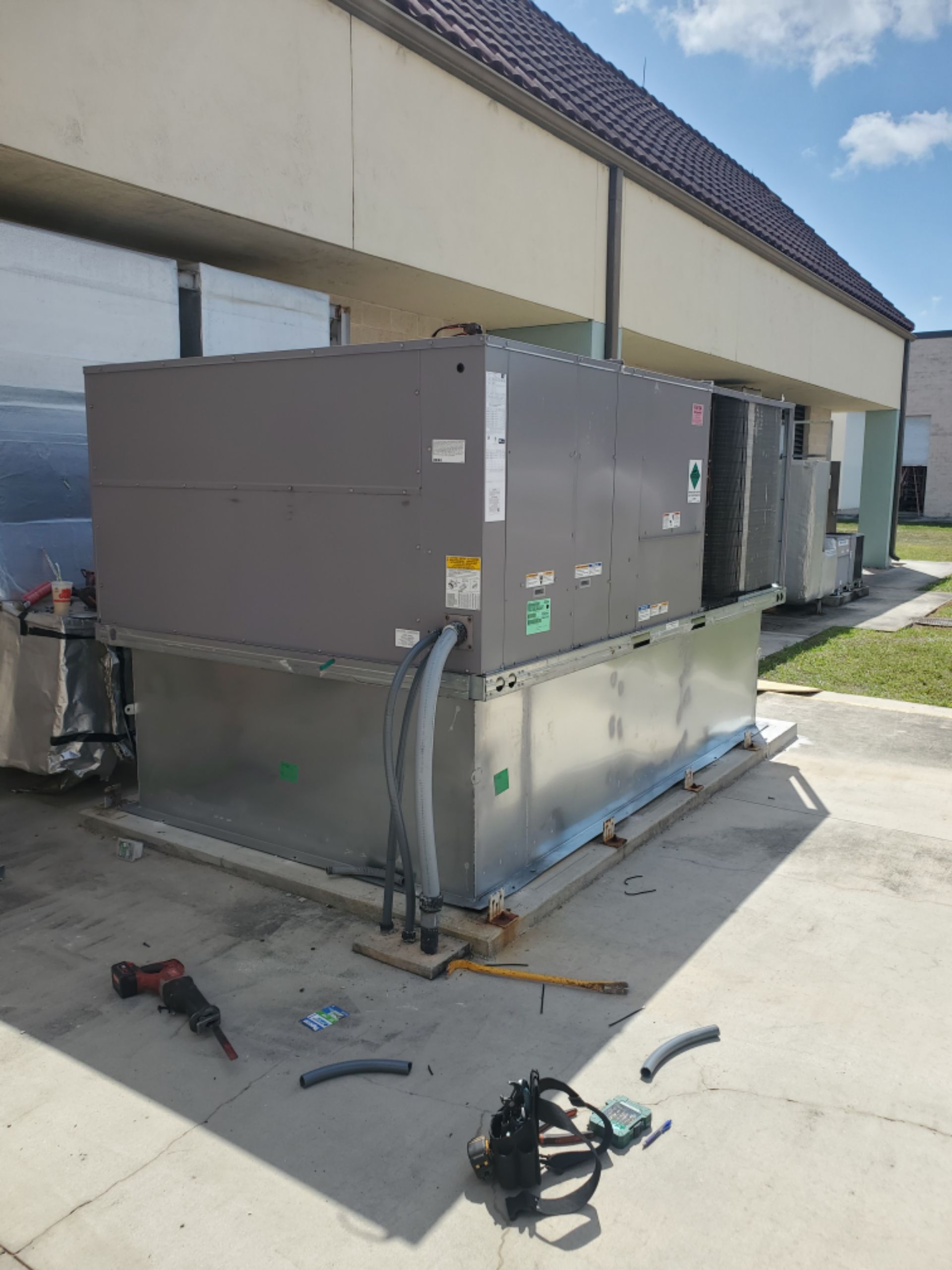 HVAC unit on a concrete slab next to a building. Tools and debris are scattered nearby.