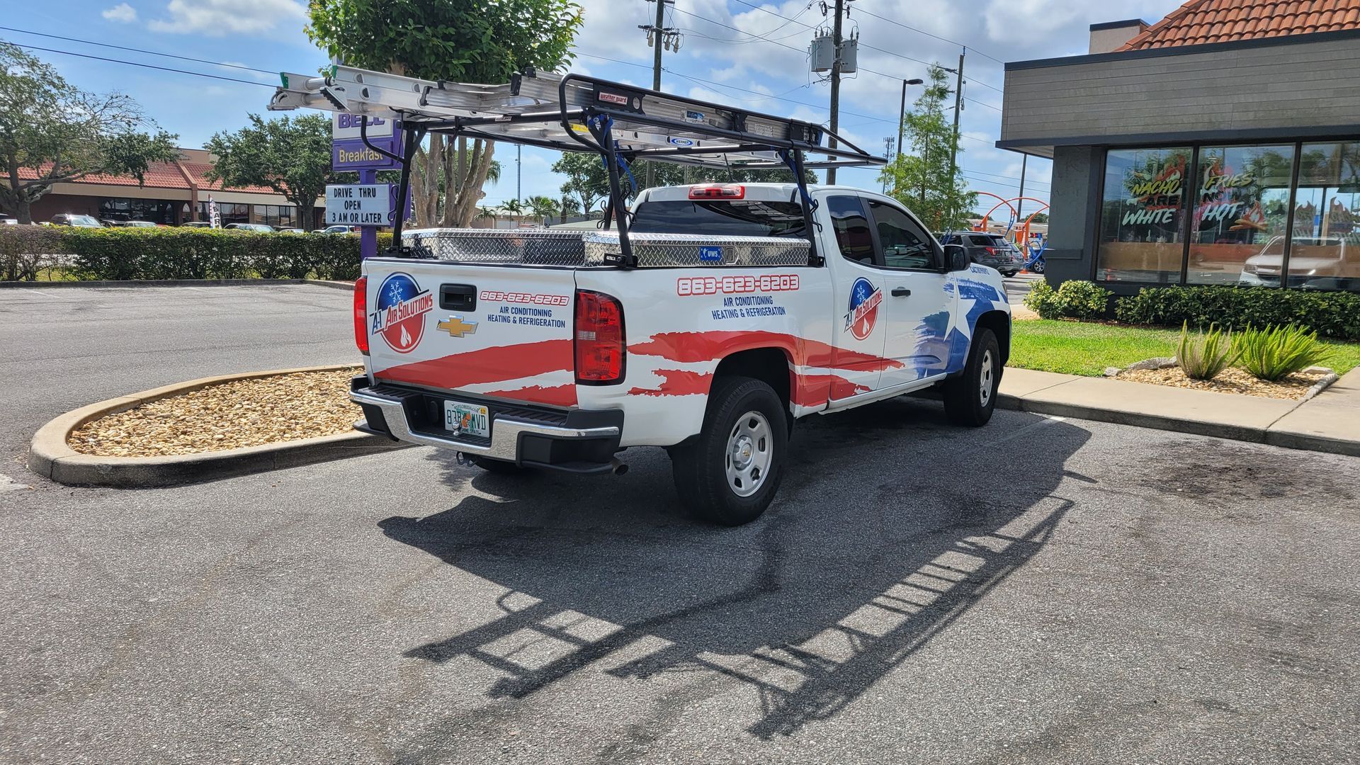 White Chevy pickup truck with ladder rack, parked in a parking lot. It has a patriotic design.