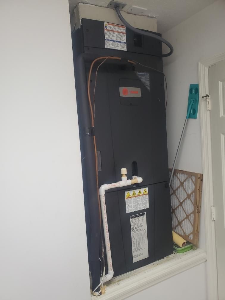 A dark HVAC unit installed in a white wall alcove; a cleaning mop and air filter are nearby.
