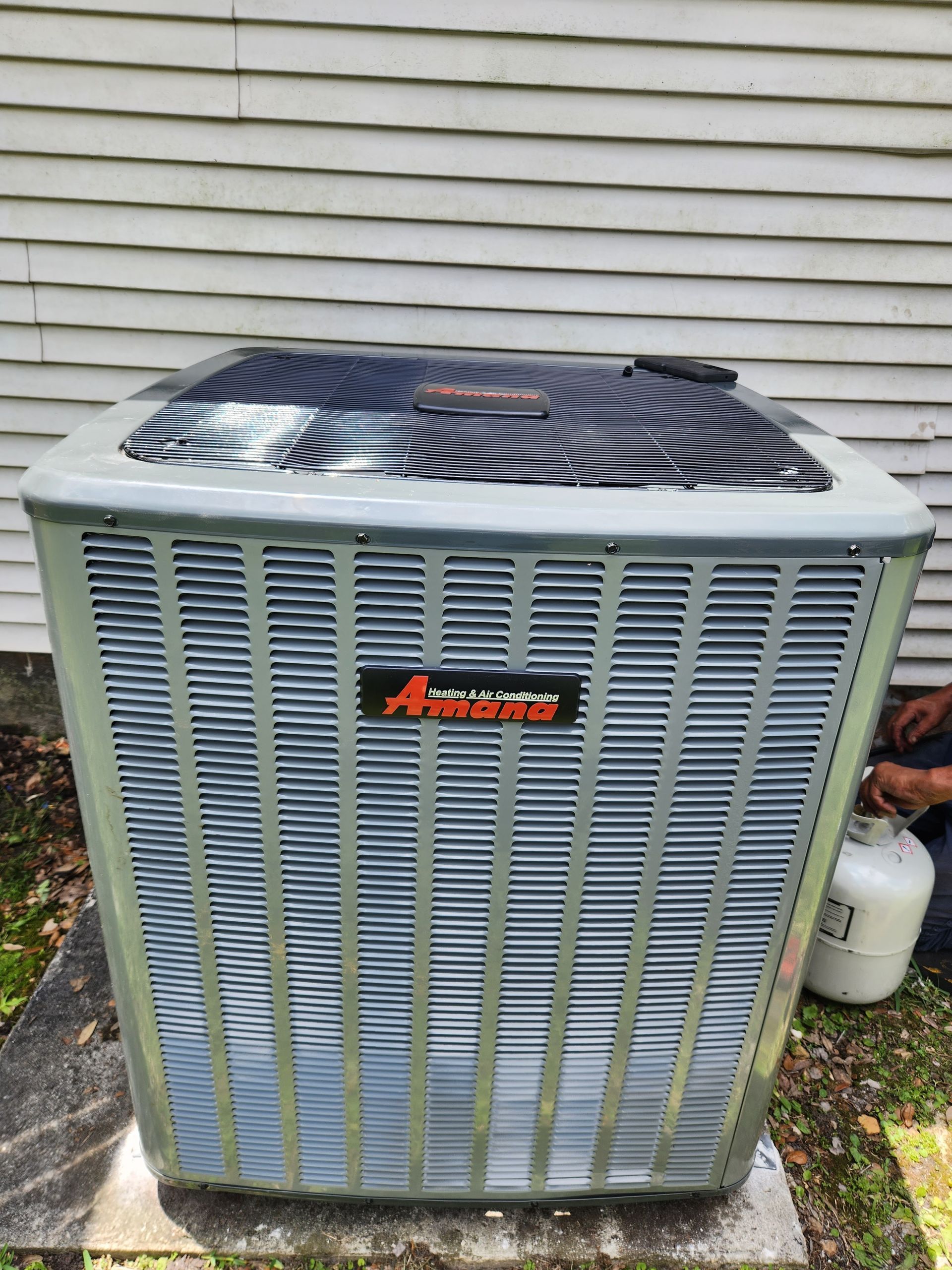 Air conditioner unit outside a building. Gray with black top, orange logo.