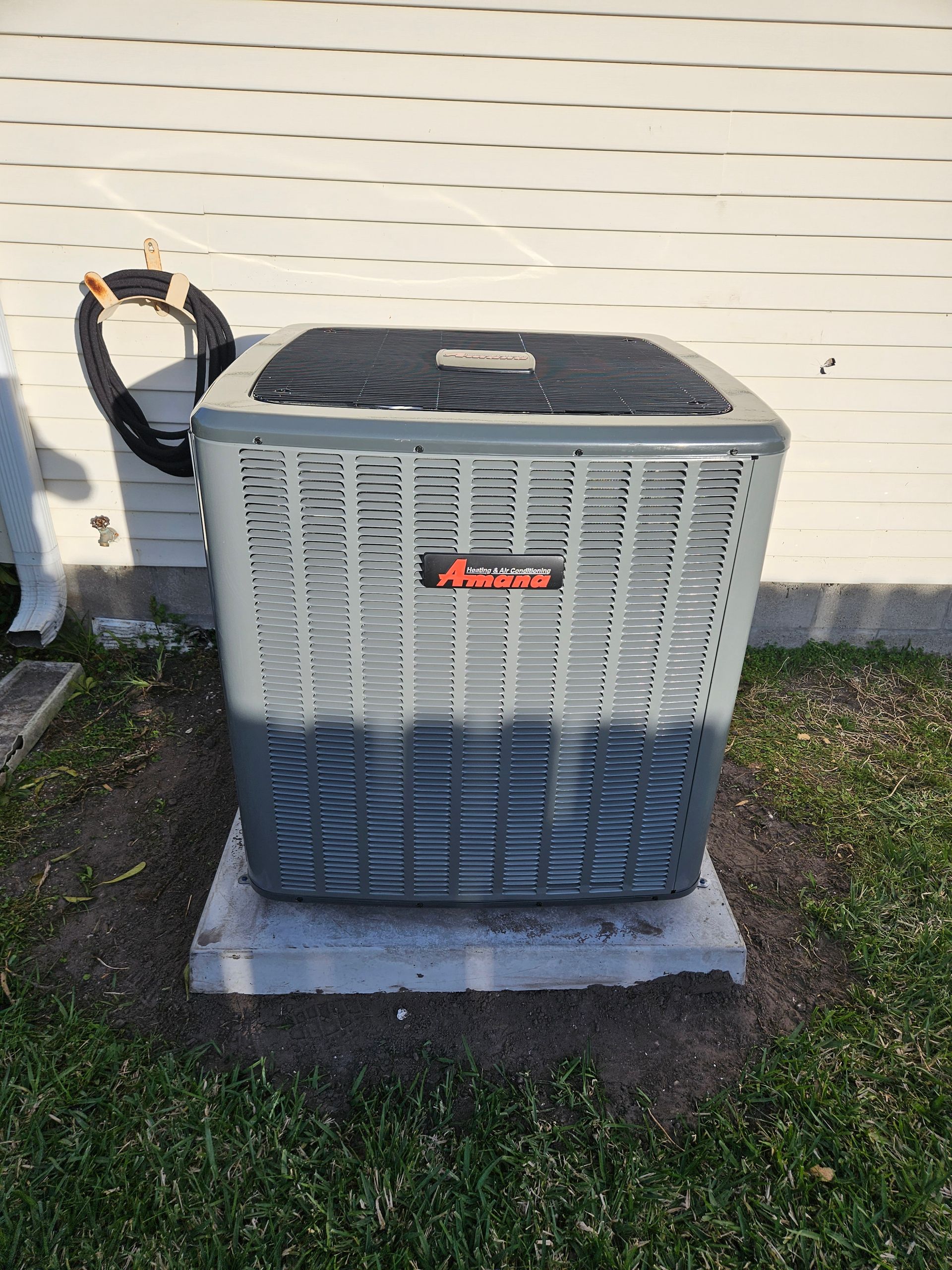 Air conditioner unit on a concrete slab, outdoor setting. Gray and black, with a protective cable.