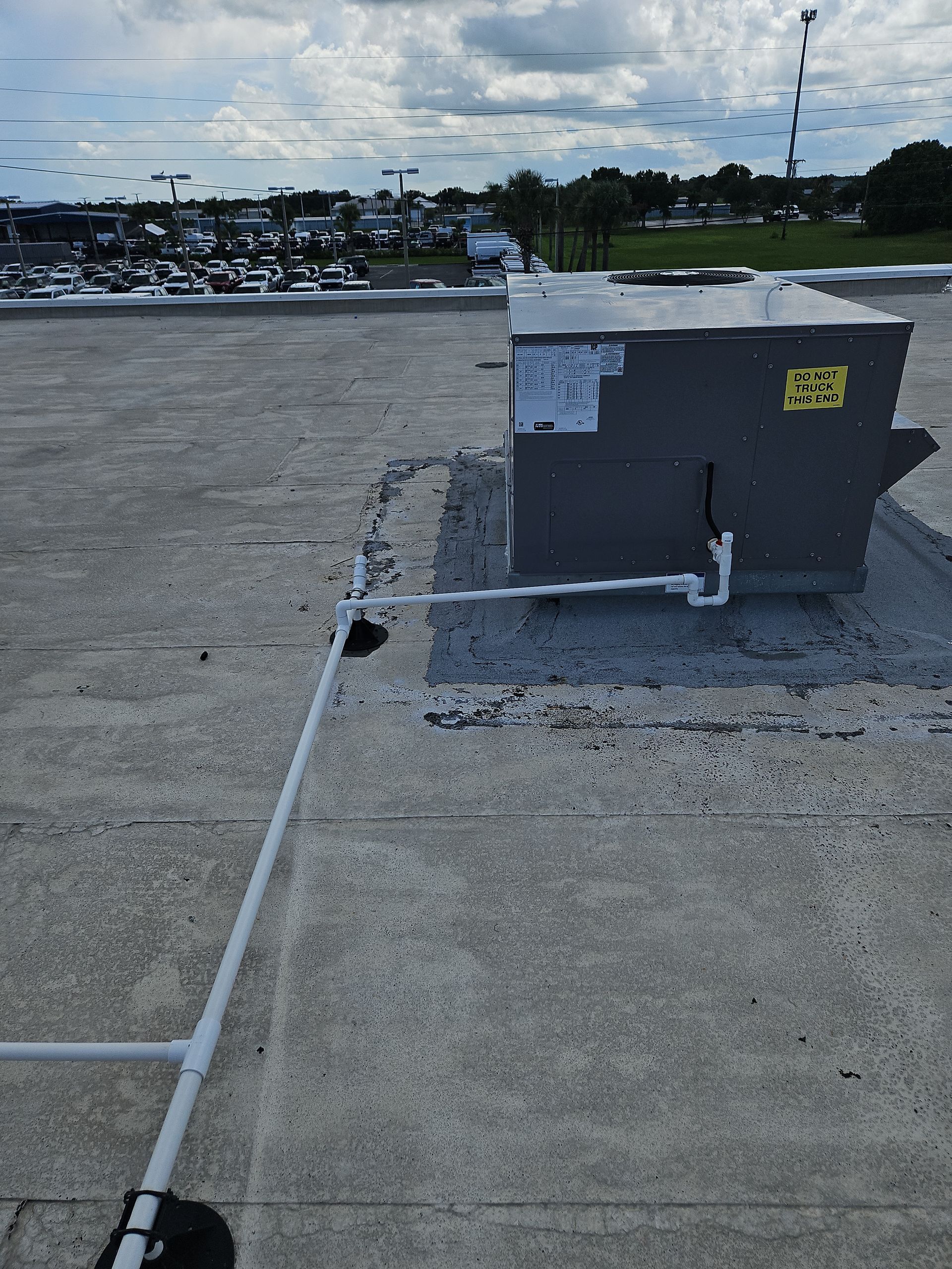 HVAC unit on a flat roof with white PVC drain pipes, cloudy sky background.