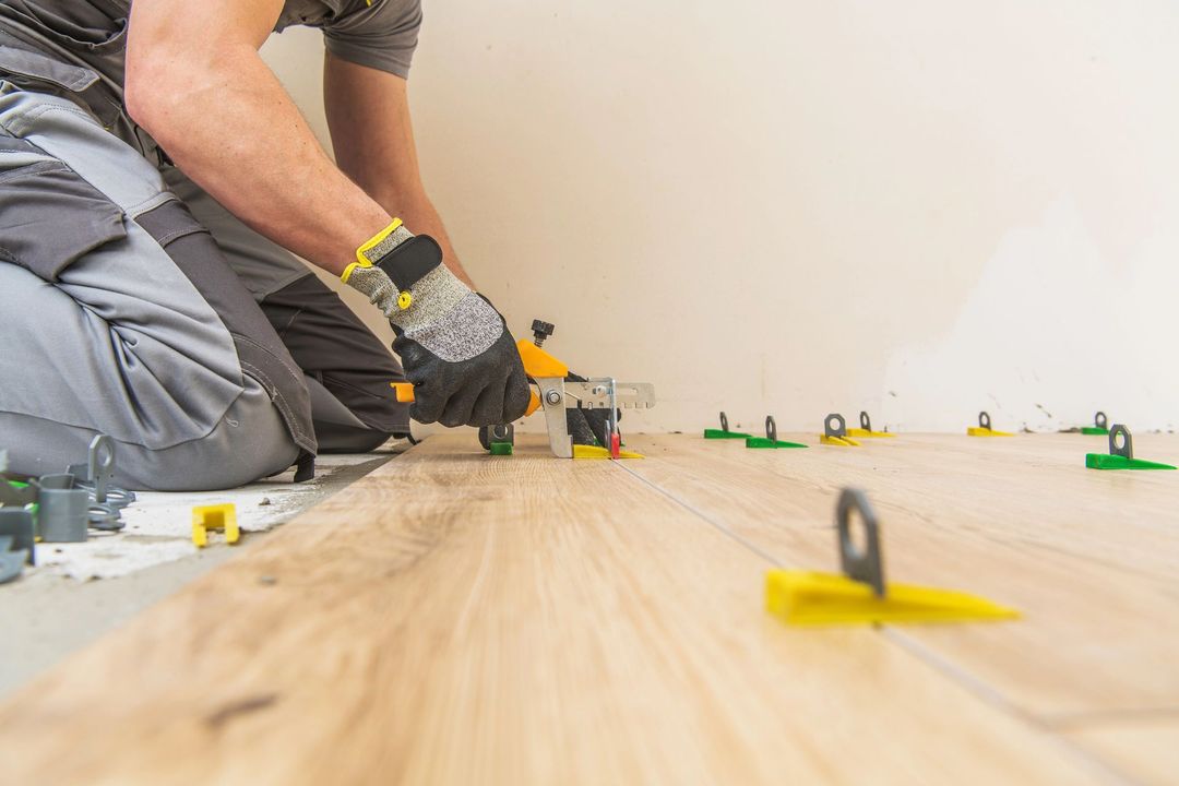 Operaio che posa piastrelle per pavimenti con distanziatori e attrezzi lungo un pavimento in legno