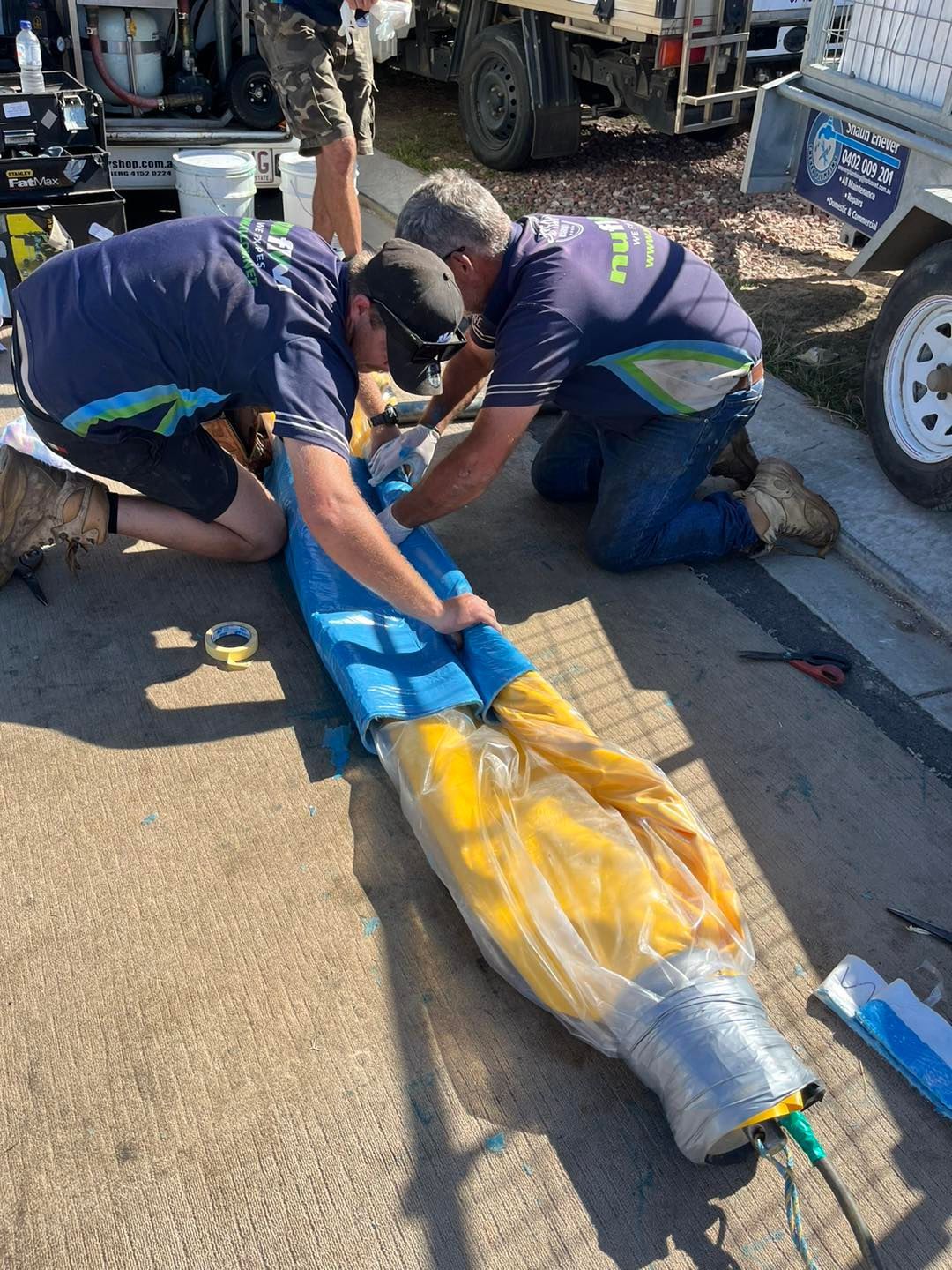 Two Men Working on A Cylindrical Object Outdoors — Nuflow Wide Bay in Bundaberg South, QLD