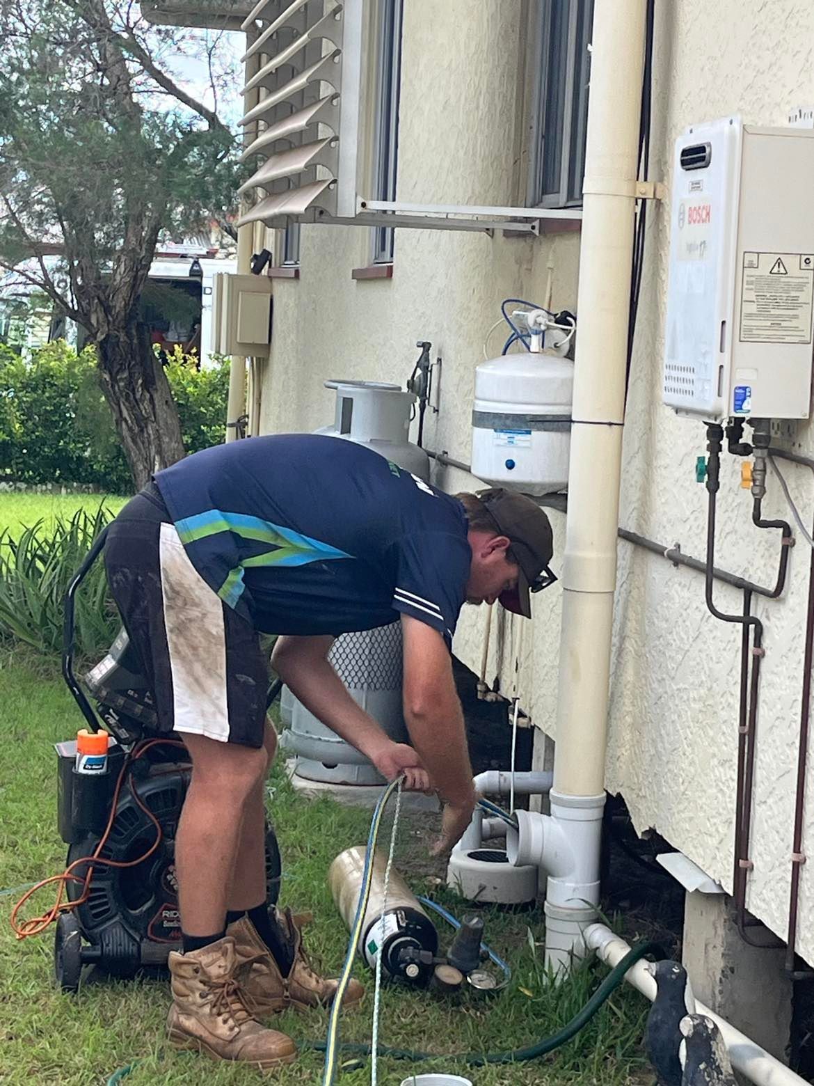 A Man Working on Plumbing Near a House — Nuflow Wide Bay in Gin Gin, QLD