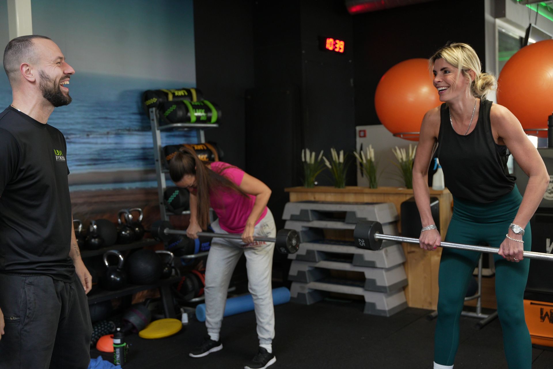 Een sportschool met gewichten en fitnessapparatuur tegen een muurschilding van een strandscène.