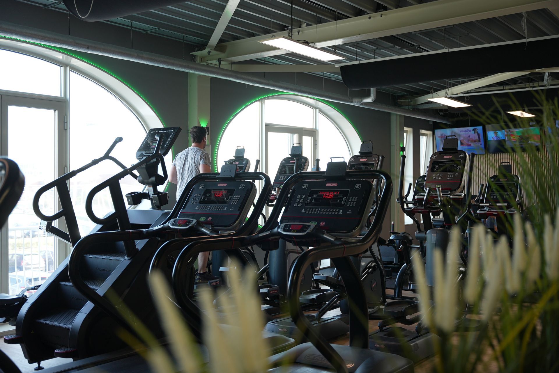 Mensen die lachen in een sportschool: een man lacht, twee vrouwen tillen gewichten met een halter, oranje oefenballen.