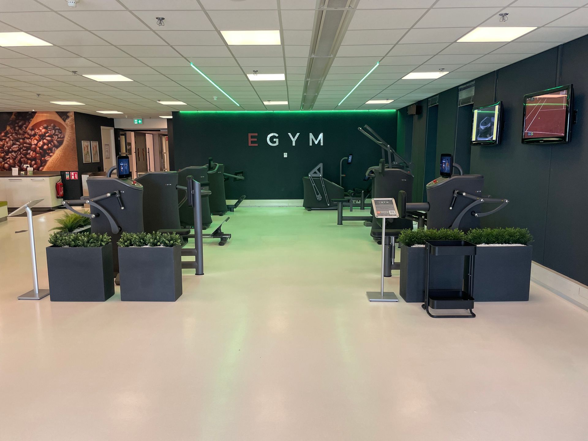 Interieur van een EGYM-fitnesscentrum met fitnessapparaten, planten en groene verlichting tegen een donkere muur.