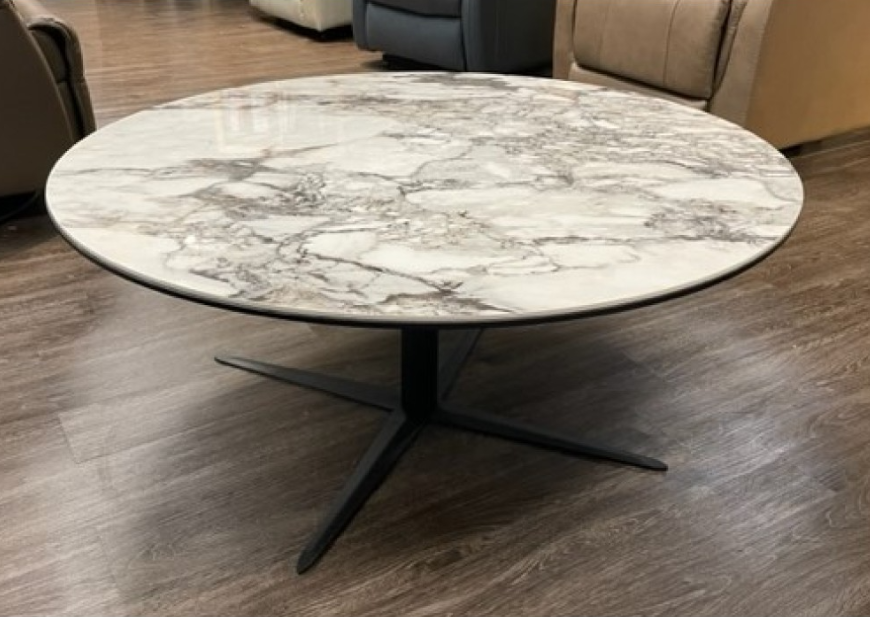 Round coffee table with marble-look top and black star-shaped base on wooden floor.