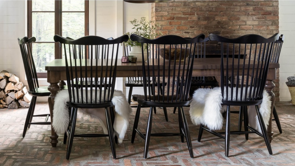 Dining room with a dark wood table, black chairs with fur throws, and a brick fireplace.
