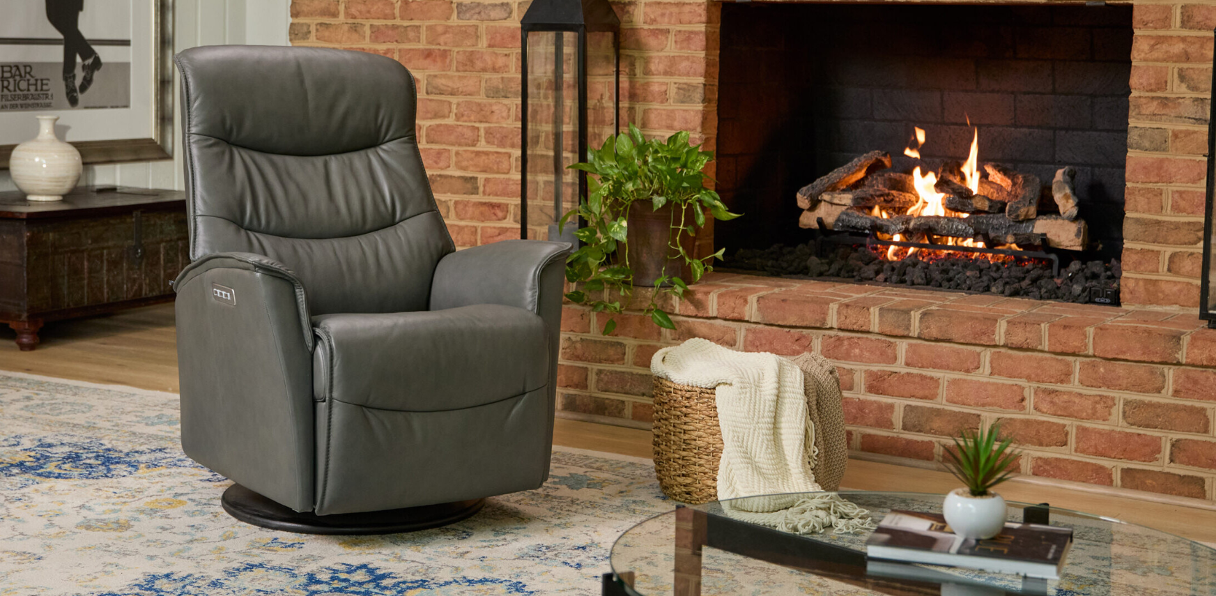 A gray leather swivel recliner in a cozy room with a lit fireplace, a brick wall, and a patterned area rug.