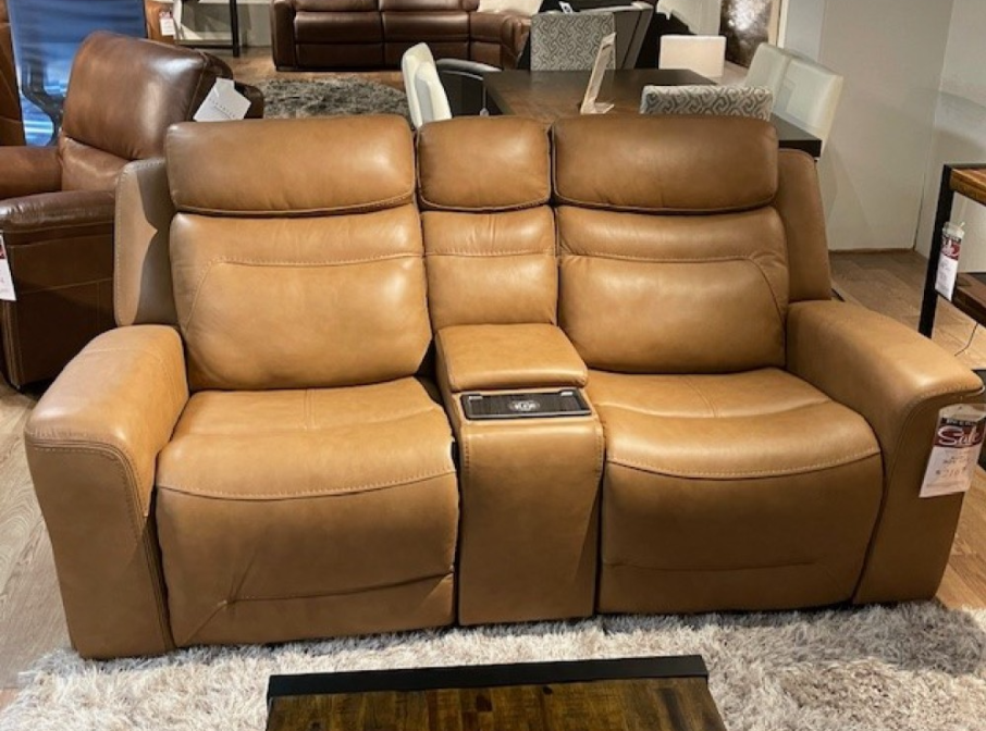 Tan leather recliner sofa with console, indoors on a rug.