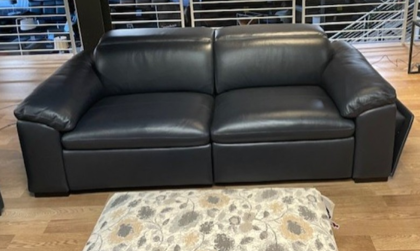 Black leather loveseat indoors, with a floral pattern ottoman in front.