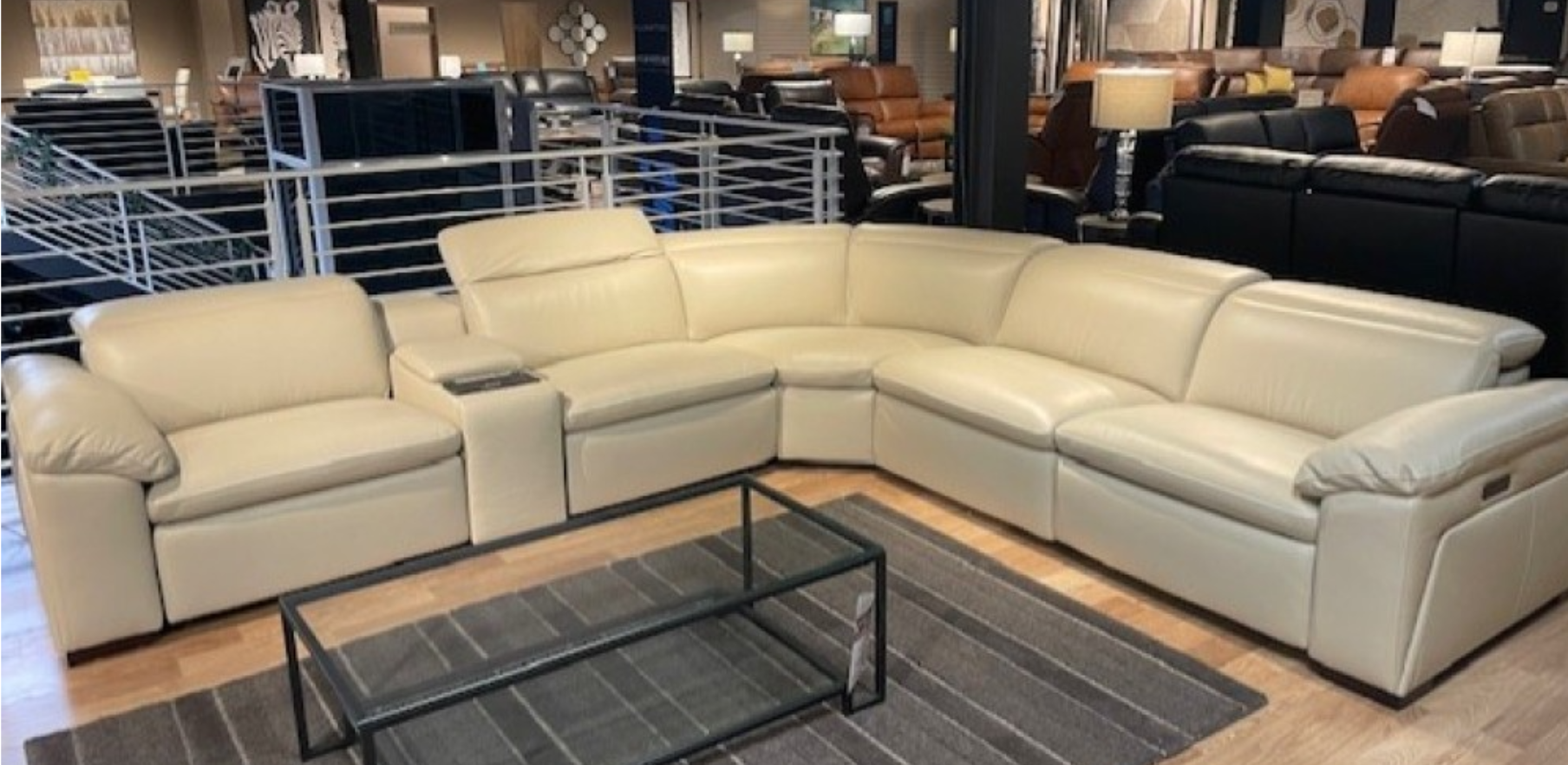 Cream-colored leather sectional sofa in a furniture store setting. Includes a built-in console and coffee table.