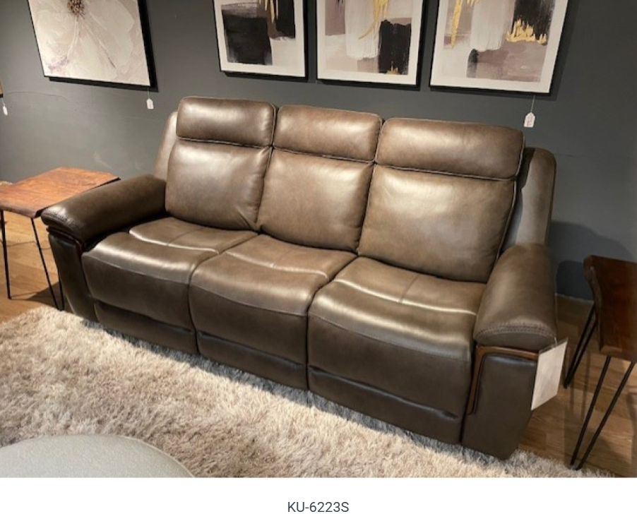 Living room furniture set: brown leather sofas and recliner, round white ottoman, beige shaggy rug, artwork.