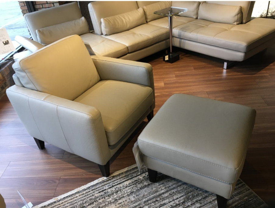 Beige leather living room furniture set, including a sofa, armchair, and ottoman, on a wooden floor.