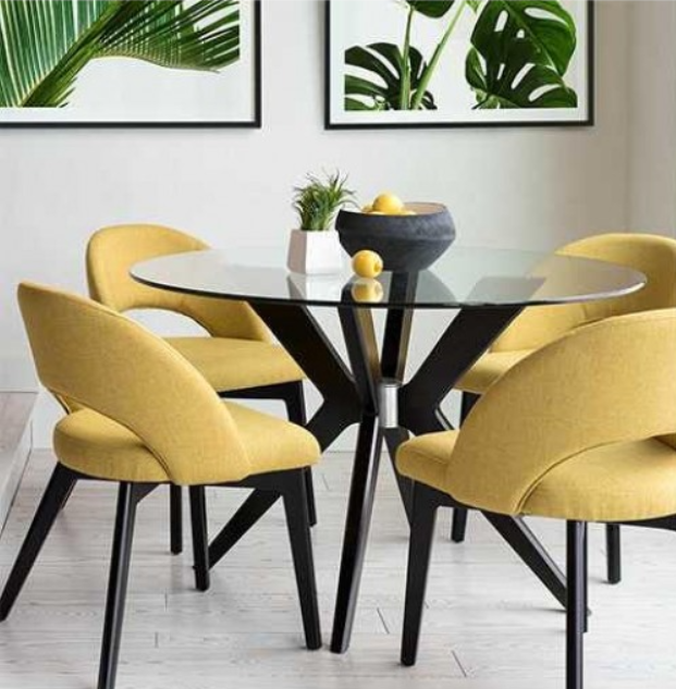 Round glass-top dining table with four yellow upholstered chairs, against a wall with framed botanical prints.