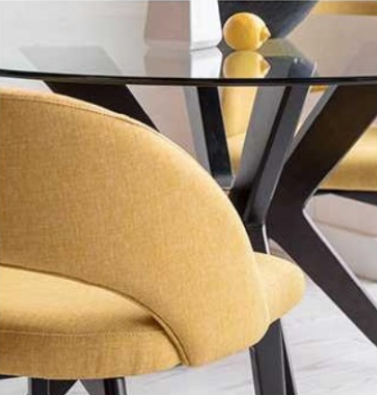 Round glass-top dining table with four yellow upholstered chairs, against a wall with framed botanical prints.