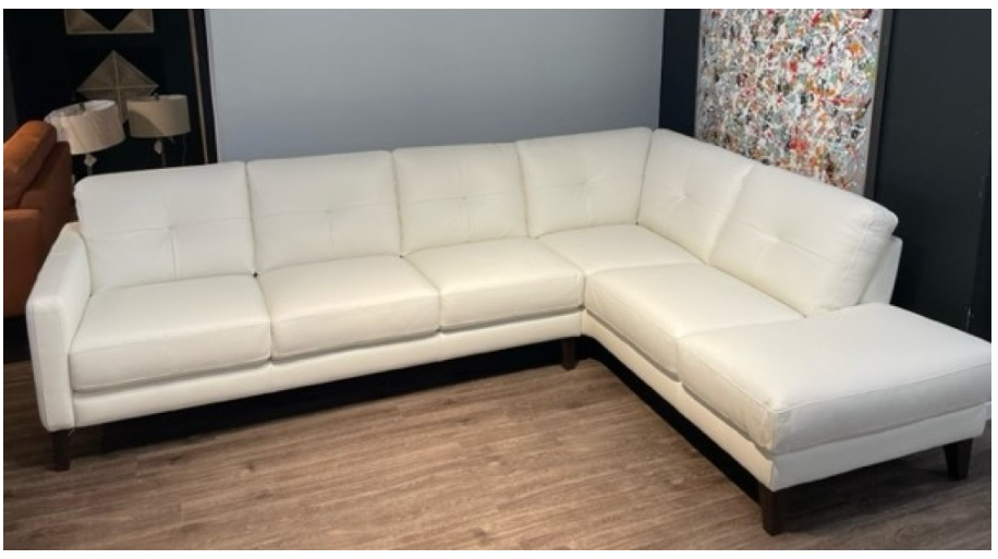 White leather sectional sofa with chaise, dark wood legs, in a room with artwork.