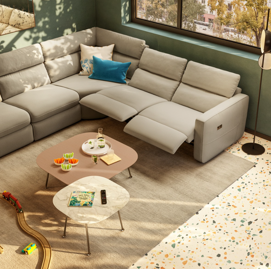A light gray sectional sofa with reclined seats sits on a rug near two nesting coffee tables and a toy train track.