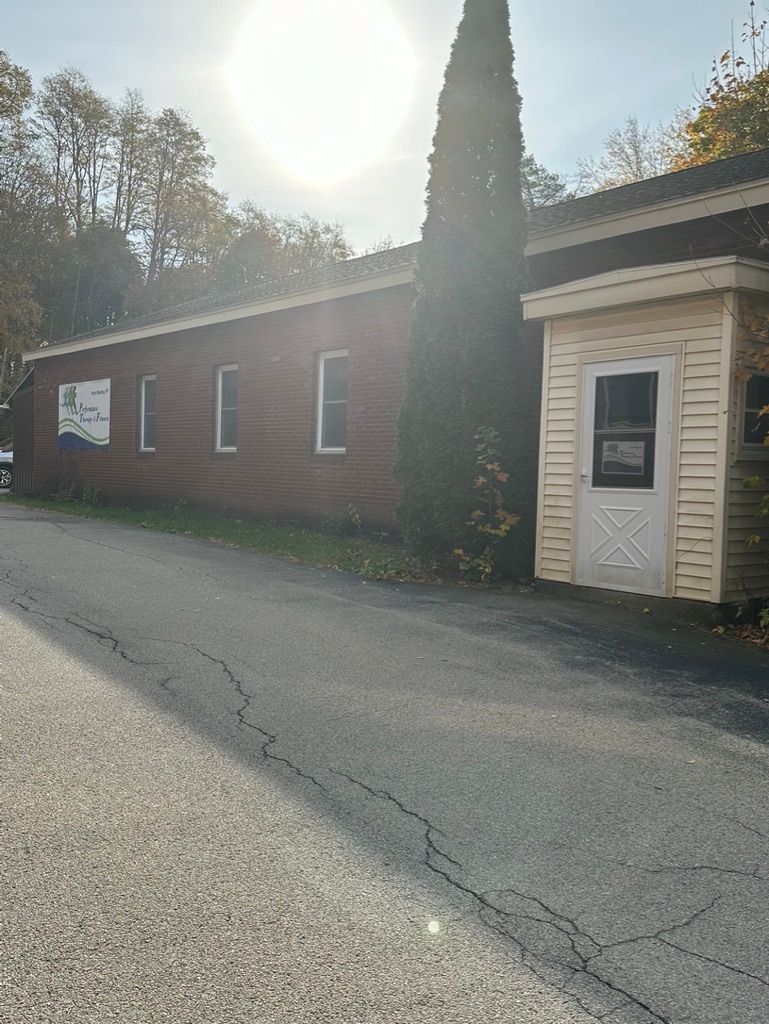 Red and tan building with white trim, asphalt road, and tall evergreen tree.