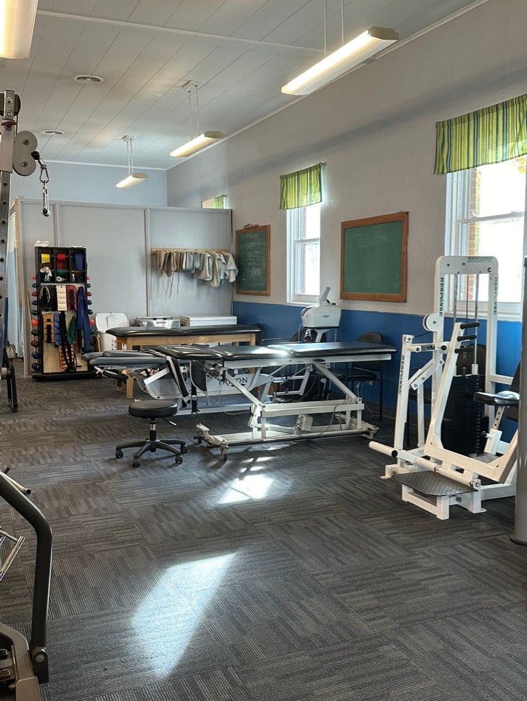 Physical therapy clinic with exercise equipment, treatment tables, and windows.