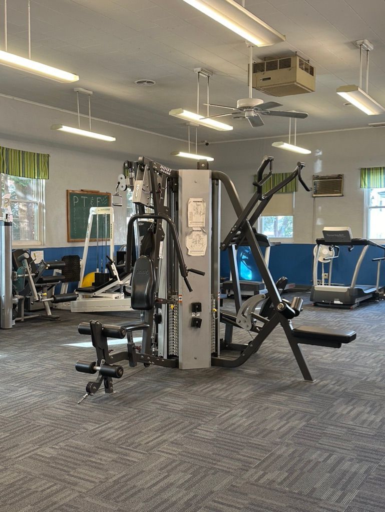 Gym interior with exercise machines, including a multi-station weight machine and treadmill. Blue walls, and a neutral carpet.