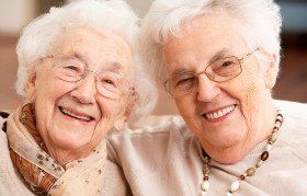 Two senior citizens with arms around each other's shoulders smiling