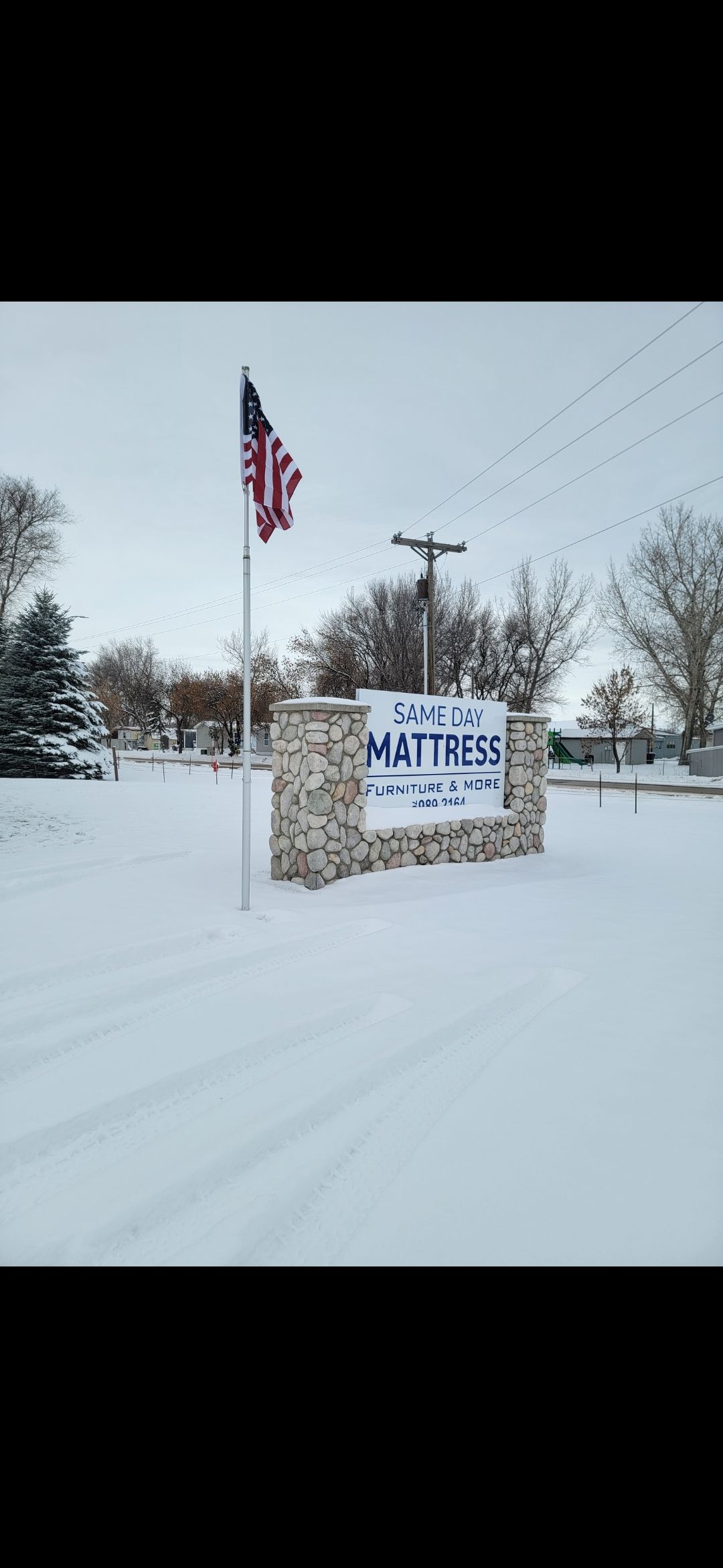 A snowy scene with a stone sign and American flag. The sign reads 