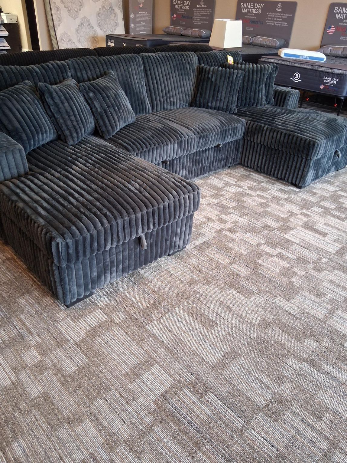 Gray corduroy sectional sofa with ottoman on patterned carpet.