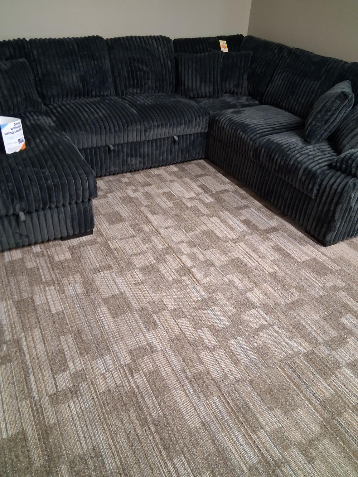 Dark blue corduroy sectional sofa on a light brown patterned carpet.