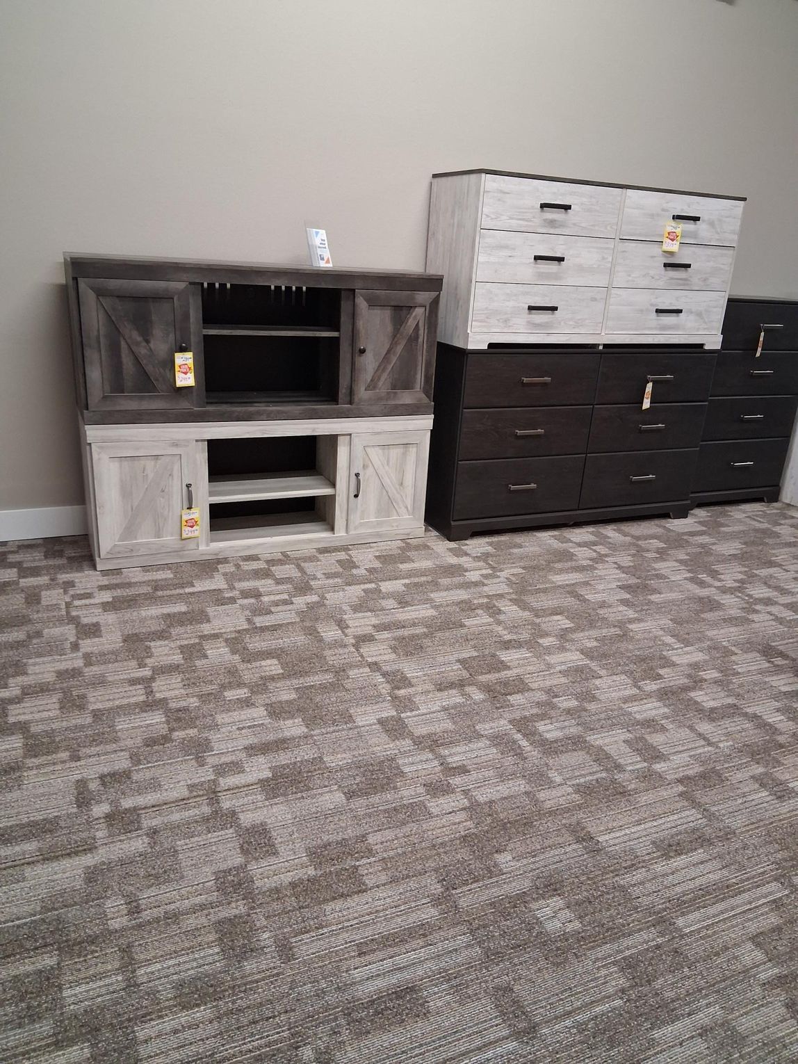 A living room furniture set, including a TV stand and a dresser, sits in front of a neutral-colored wall on a patterned carpet.