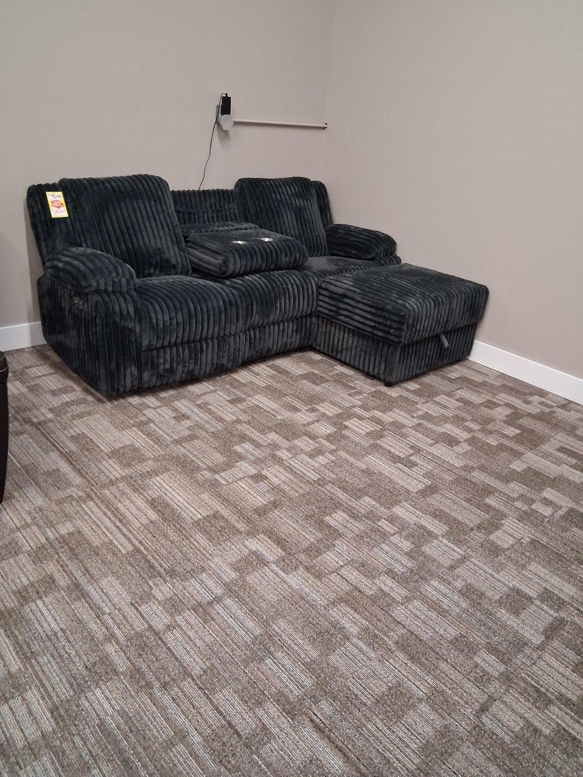 Gray sectional sofa with cup holders in a room with patterned carpet and beige walls.