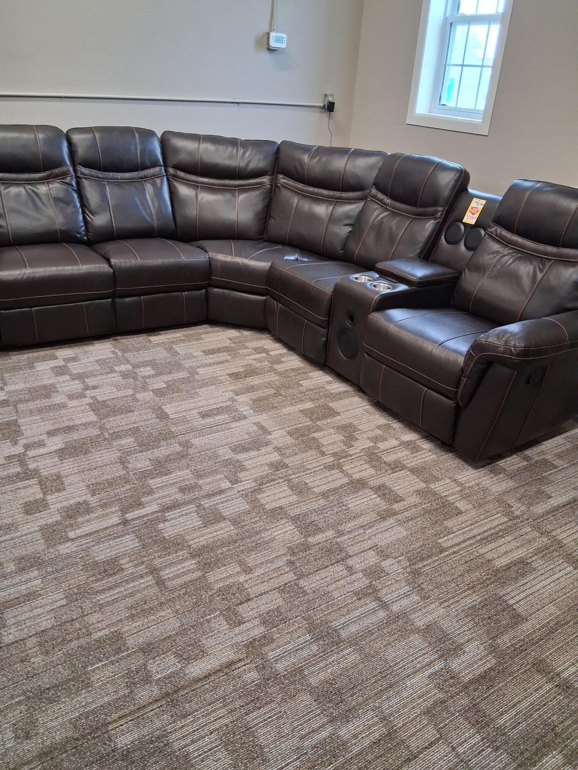 Brown leather sectional sofa with cup holders, on patterned carpet, near a window.