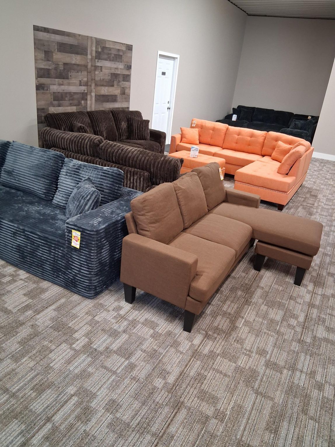Various sofas in a showroom: blue, brown, orange and black. Carpeted floor, neutral walls.