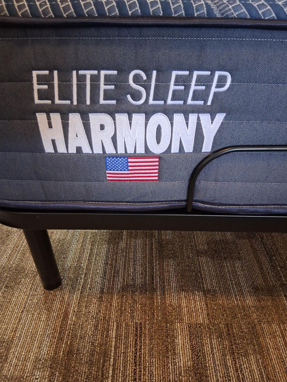 Elite Sleep Harmony mattress with the US flag, set on a black metal bed frame.