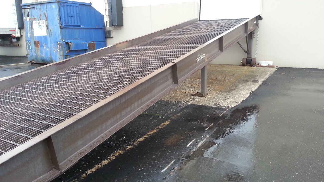 A metal ramp leading to a building with a blue dumpster in the background