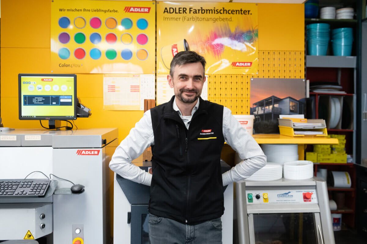 Ein Mann steht in einer Kaffeerösterei neben Geräten und farbenfrohen Produktauslagen.