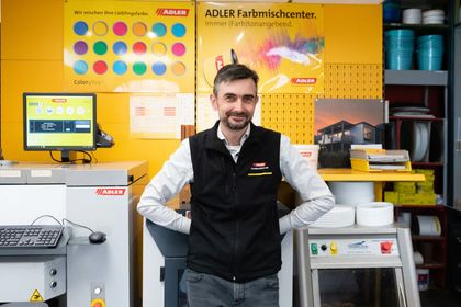 Ein Mann steht in einer Kaffeerösterei neben Geräten und farbenfrohen Produktauslagen.