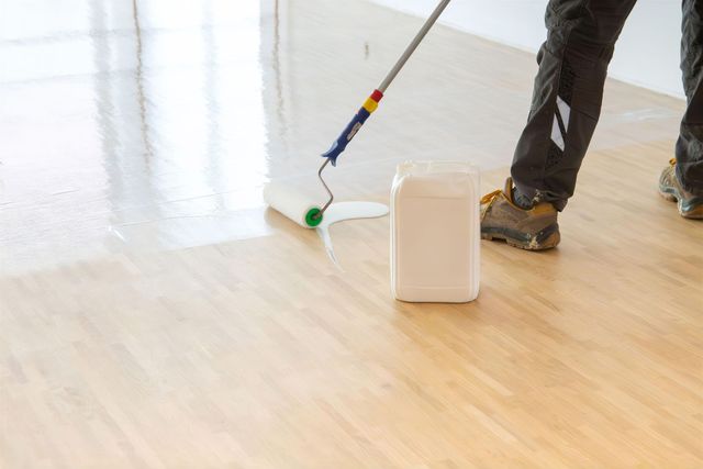 Eine Person wischt einen hellen Holzboden neben einem kleinen weißen Eimer oder Behälter.