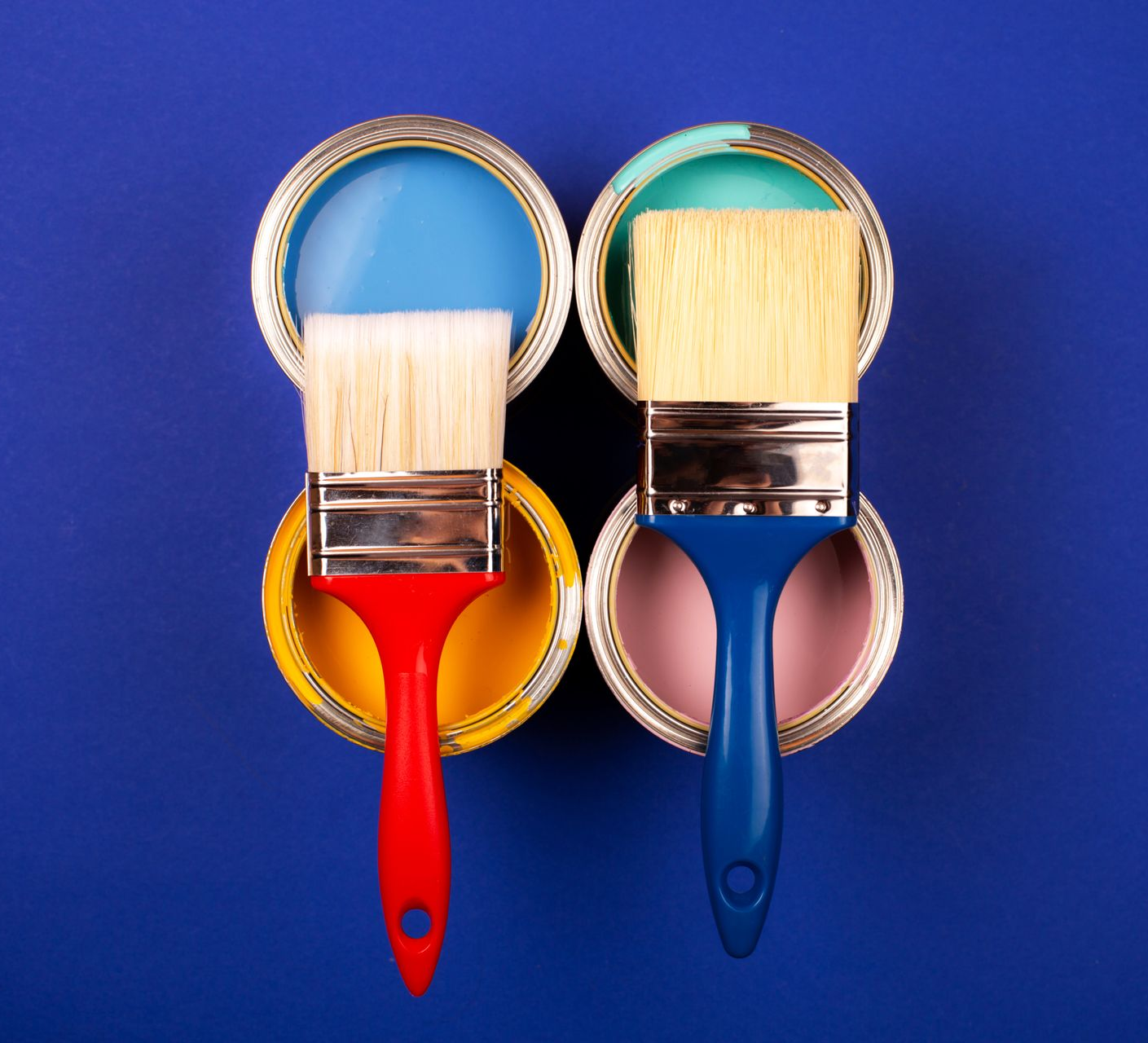 Vier Pinsel mit roten, blauen, gelben und rosafarbenen Griffen sind auf blauem Hintergrund in einem Quadrat angeordnet.