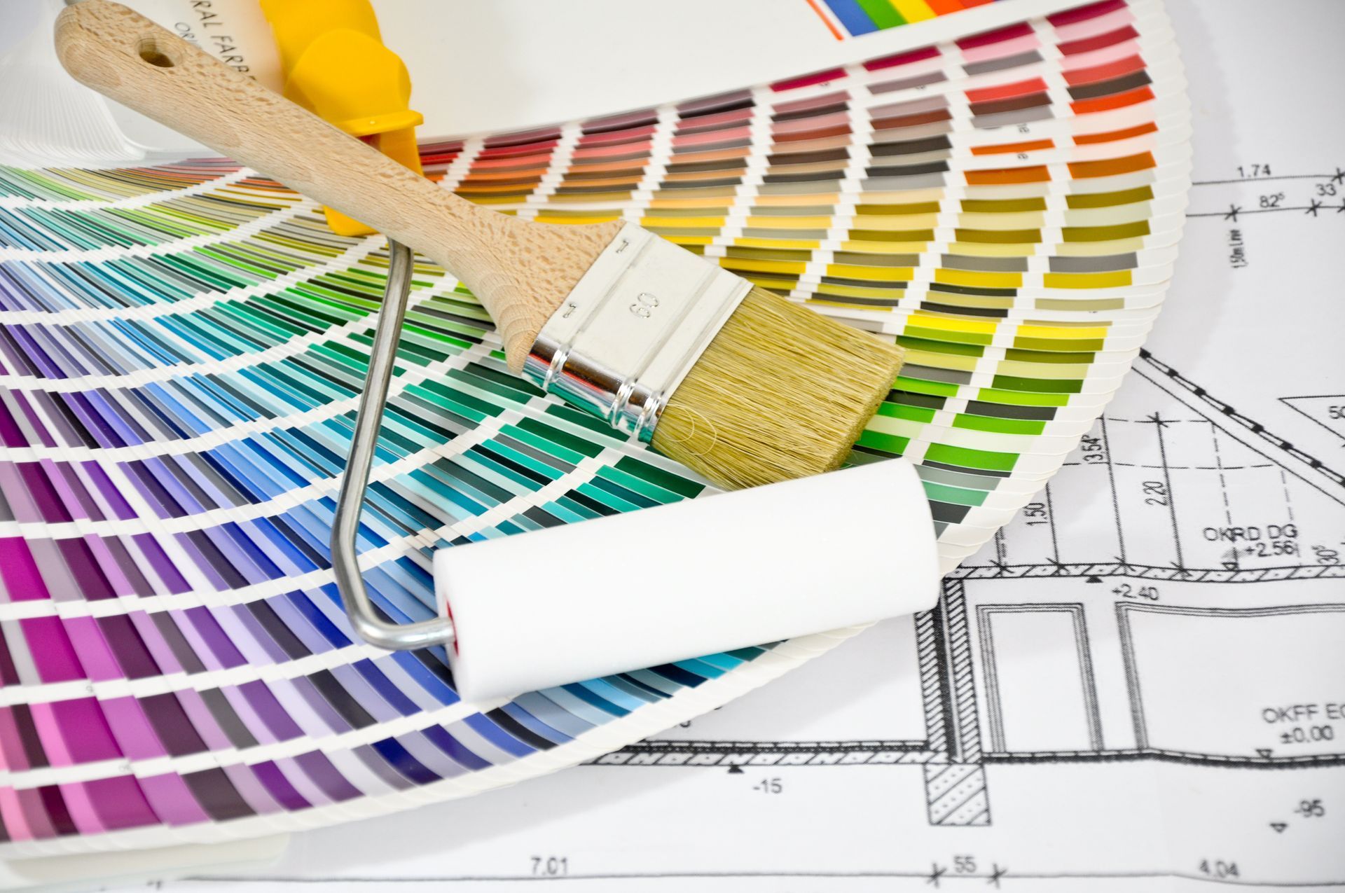 Farbmuster und Malwerkzeuge auf einem Architekturplan, mit Pinsel und Farbrolle.