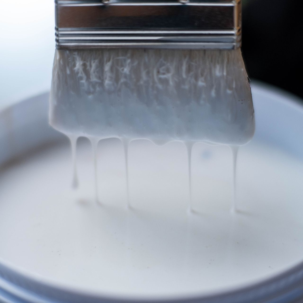 Weiße Farbe tropft von einem Pinsel auf eine weiße Oberfläche